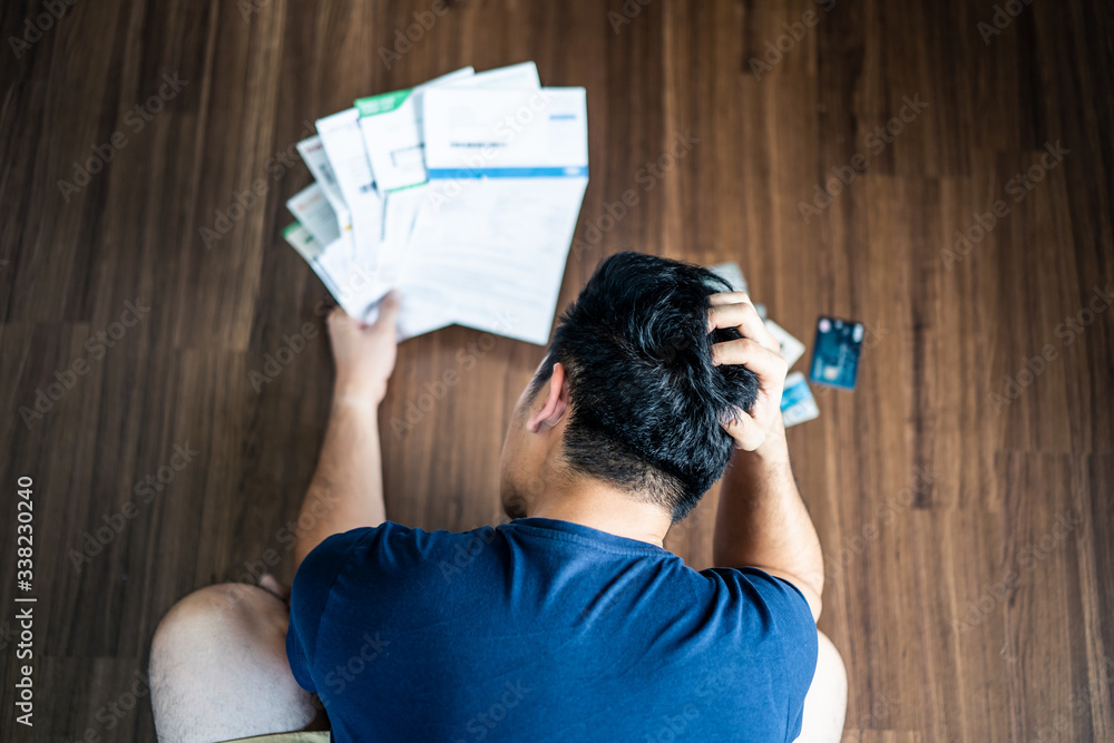 © Kawee - Top view of stressed young Asian man hands holding the head trying to find money to pay credit card debt and all loan bills. Financial problem from coronavirus or covid-19 outbreak crisis concept.