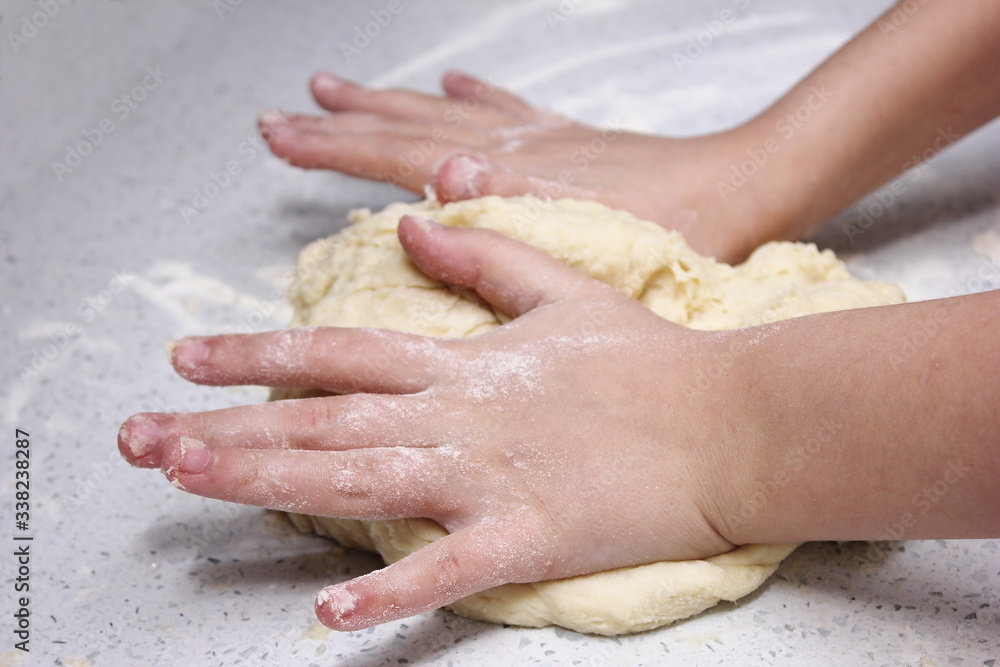 Children's hands knead a piece of dough. The process of kneading the dough