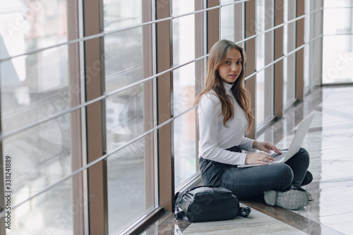 attractive girl working with laptop and things in airport terminal or office on floor. travel atmosphere or alternative work atmosphere. freelancer student travels to business meeting.