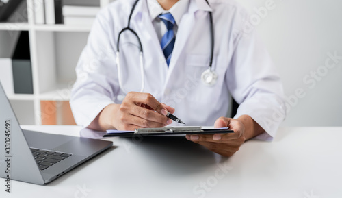 Doctor holding the patient report file to assess symptoms on the desk.