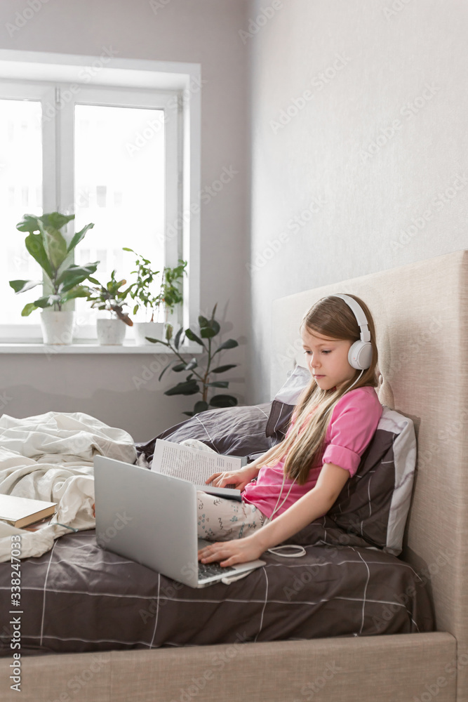 School girl studying at home on the bed with laptop notebook and listens to an online lesson. Distance learning online education. Social distance during quarantine, online education concept. copyspace School girl studying at home on the bed with laptop notebook and listens to an online lesson. Distance learning online education. Social distance during quarantine, online education concept. copyspace