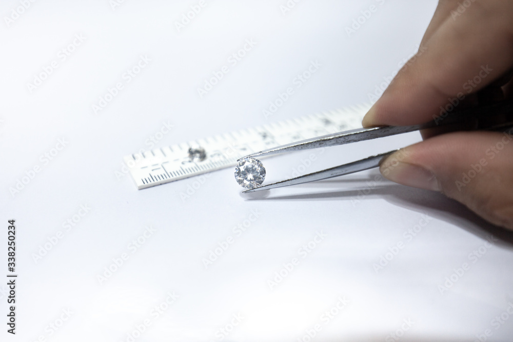 Diamond Scale Ruler Hand holding a diamond with linear scale, tweezers and a pile of ...