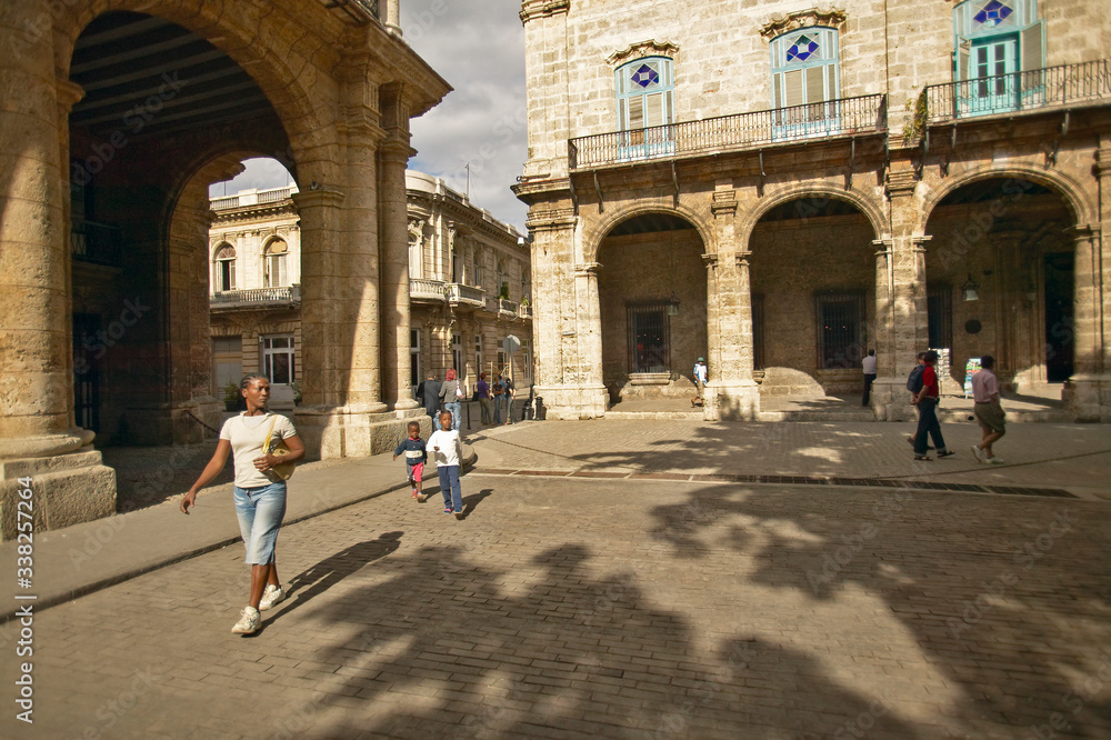 Obraz premium A Cuban woman and child walking through an old Plaza in Old Havana, Cuba with archways