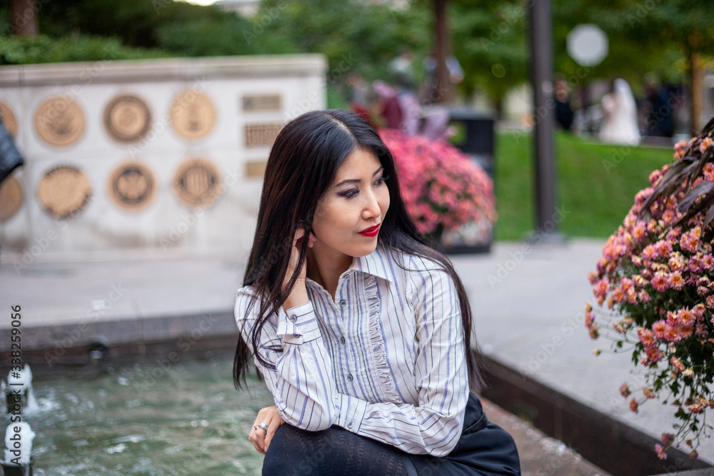 Fototapeta premium happy Asian business woman with long black hair wearing a trendy corporate shirt and skirt is sitting confidently at an outdoor park enjoying the view of Chicago downtown