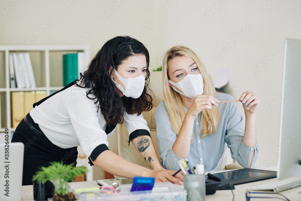 Executive mentor in protective medical mask explaining colleague how to use corporate software or helping with difficult assignment