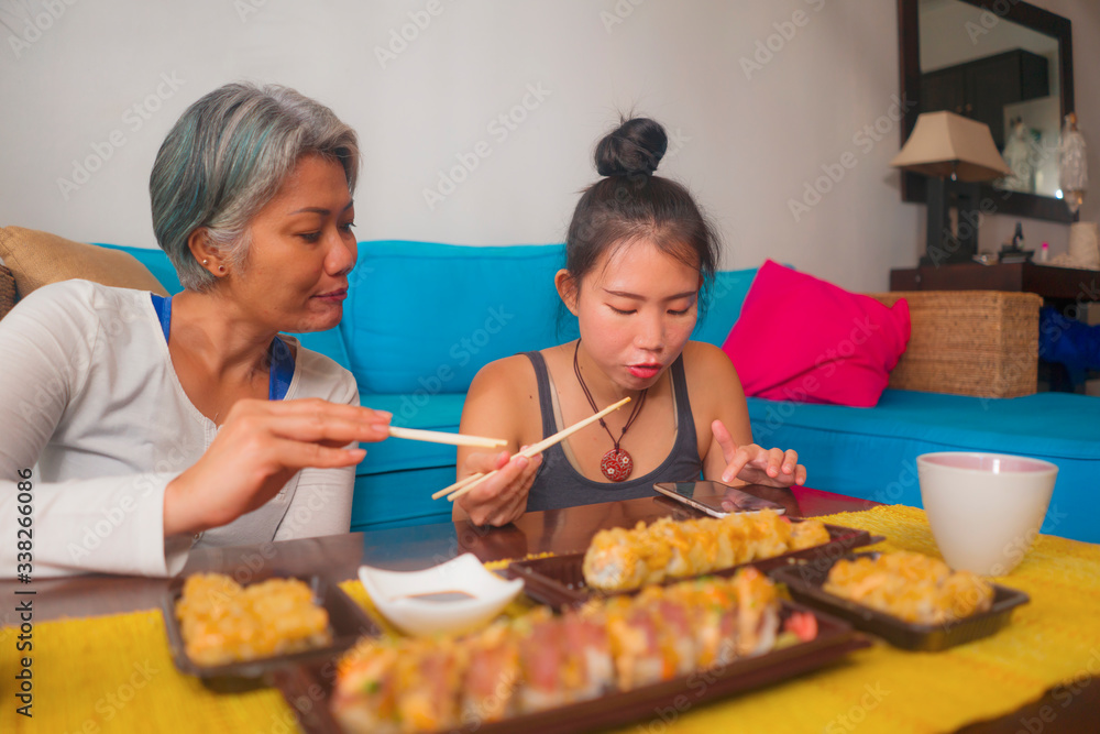 Asian female friends having Japanese sushi for lunch - happy and attractive woman and her girlfriend eating sushi rolls at home enjoying together healthy delicious food