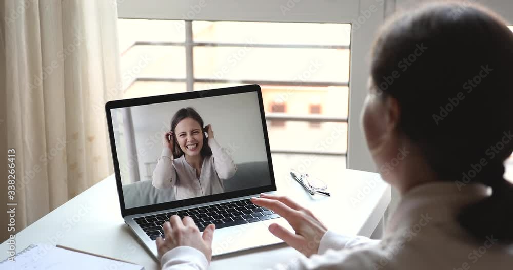 Two happy girls teen friends laughing communicating by webcam using video conference call app. Social distancing friendship relationship concept, virtual chat on laptop screen. Over shoulder view Two happy girls teen friends laughing communicating by webcam using video conference call app. Social distancing friendship relationship concept, virtual chat on laptop screen. Over shoulder view