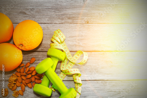 Lots of oranges, dumbbells, measuring tape on a wooden textured background. Fitness, sports nutrition. photo