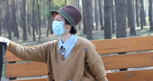 A stylish woman wearing mask and gloves to defened her from coronavirus. Using electric scooter in city and park to be in safe.