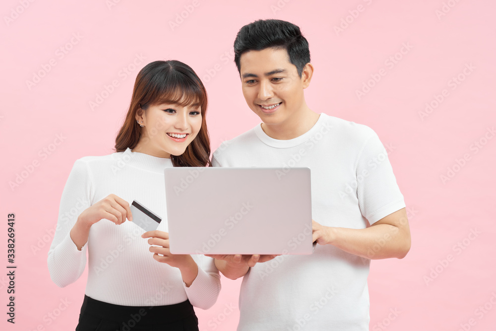 Great credit offer. Cheerful asian couple shopping online on laptop with bank card on pink studio background Great credit offer. Cheerful asian couple shopping online on laptop with bank card on pink studio background