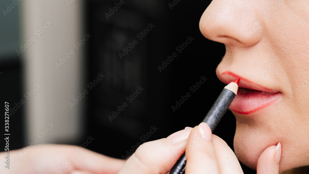 make up artist paints lips with a lip pencil to a woman in a beauty salon