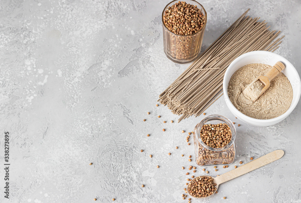 Φωτογραφία Organic uncooked buckwheat grains in glasses, buckwheat flour in a bowl and dried buckwheat soba noodles, light grey concrete background