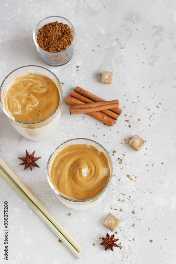 Fototapeta premium Iced Dalgona coffee in tall glass with spices. A trendy fluffy creamy whipped coffee. Korean coffee drink. Light grey concrete background.