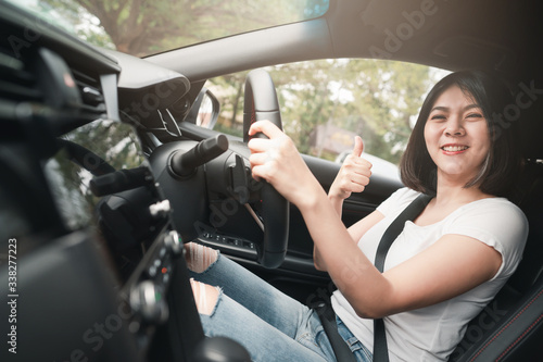 Happy smiling asian woman driving in her new car with confident showing thumb up