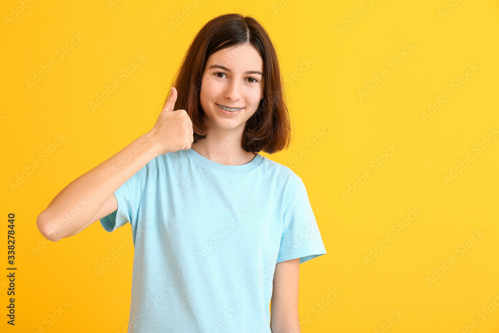 Teenage girl with dental braces showing thumb-up gesture on color background Teenage girl with dental braces showing thumb-up gesture on color background