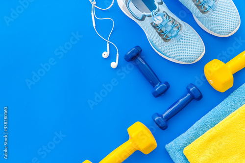 Fototapeta Naklejka Na Ścianę i Meble -  Fitness set with sneakers, dumbbells, towel on blue background top view copy space