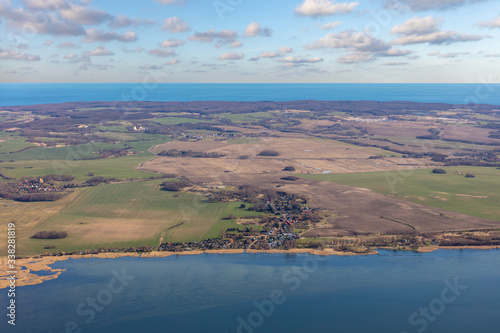 An aerial view of the northern part of the German island of Rügen in the sunshine. In the foreground is a lagoon and in the background the Baltic Sea. The place belongs to the community Glowe.