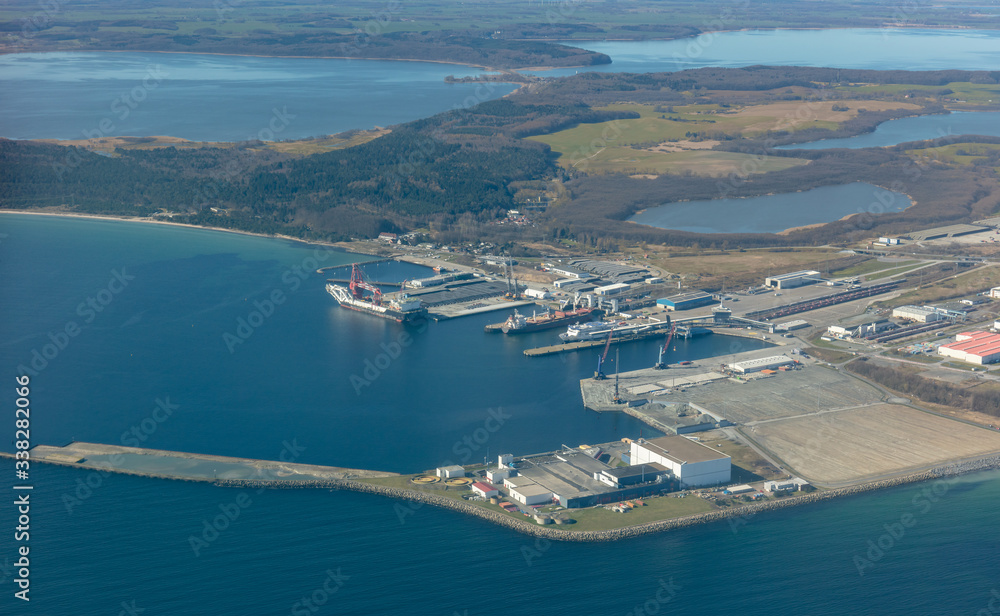 An aerial view of the industrial and ferry port of Mukran on the German island of Rügen in the Baltic Sea. There is a large industrial ship and a ferry in the harbor. Lagoons can be seen at the back.