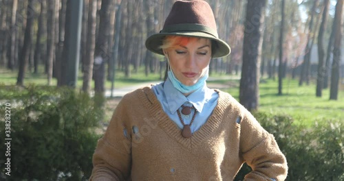 A stylish woman wearing mask and gloves to defened her from coronavirus. Using electric scooter in city and park to be in safe.