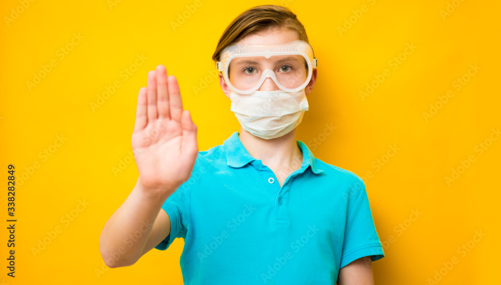 Teen boy wearing a medical protective mask against the Coronavirus Covid 19, showing stop hands gesture to stop the infectious virus outbreak. Concept of stop infection epidemic virus symptoms Teen boy wearing a medical protective mask against the Coronavirus Covid 19, showing stop hands gesture to stop the infectious virus outbreak. Concept of stop infection epidemic virus symptoms