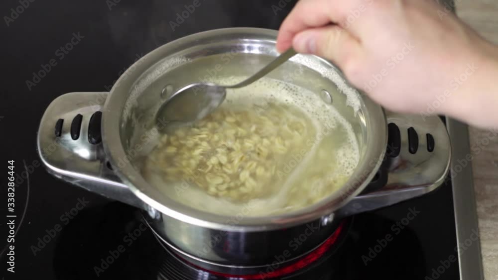 Caucasian right hand stirs vegan oatmeal cooking on stove top with silver spoon Caucasian right hand stirs vegan oatmeal cooking on stove top with silver spoon
