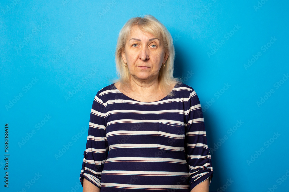 Portrait of an old friendly woman with a serious face in a casual t-shirt on an isolated blue background. Emotional face Portrait of an old friendly woman with a serious face in a casual t-shirt on an isolated blue background. Emotional face