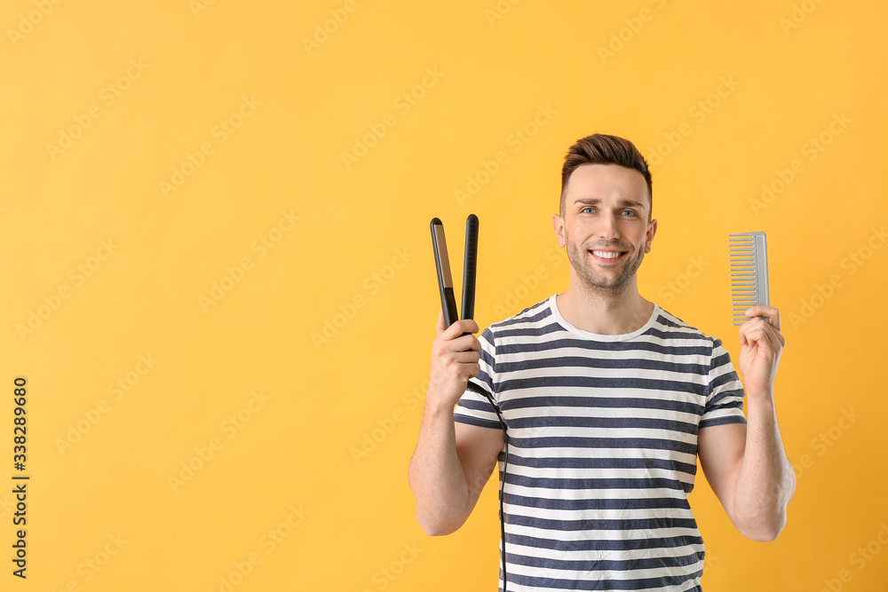 Handsome young man with flattening iron and comb on color background