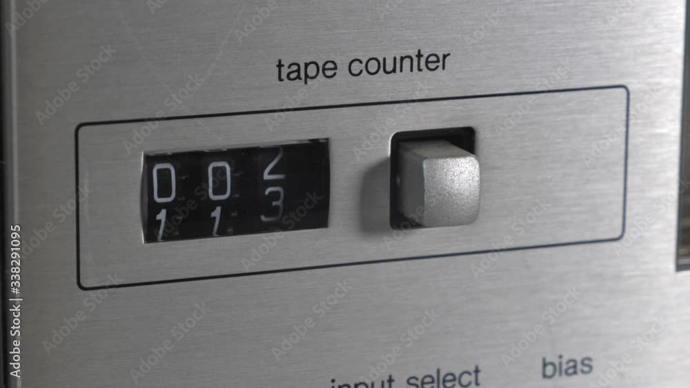 Side perspective of stereo hifi casette tape counter counting up with black digit numbers ticking over and silver metal button off to side. Side perspective of stereo hifi casette tape counter counting up with black digit numbers ticking over and silver metal button off to side.