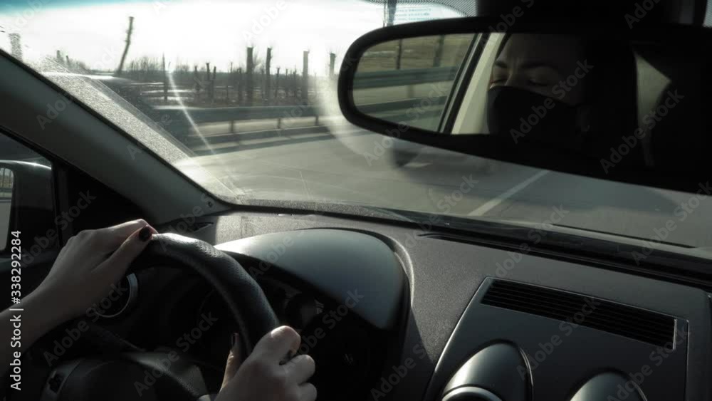 reflection of a woman wearing a face mask Covid-19 in a rearview mirror of a car while driving in a traffic jam in the evening during coronavirus reflection of a woman wearing a face mask Covid-19 in a rearview mirror of a car while driving in a traffic jam in the evening during coronavirus