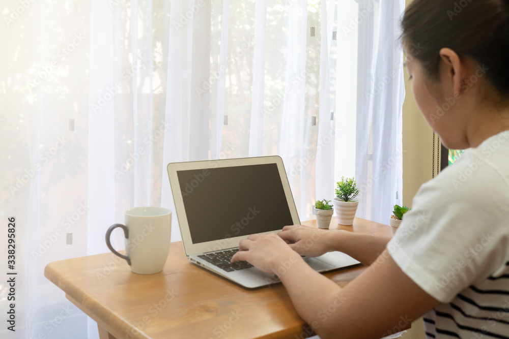 Fototapeta premium A young asian woman using computer to work from home in the living room in the morning during covid-19 or coronavirus pandemic