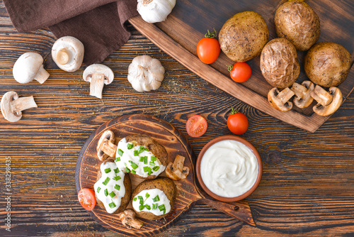 Tasty baked potato with sour cream, vegetables and mushrooms on table