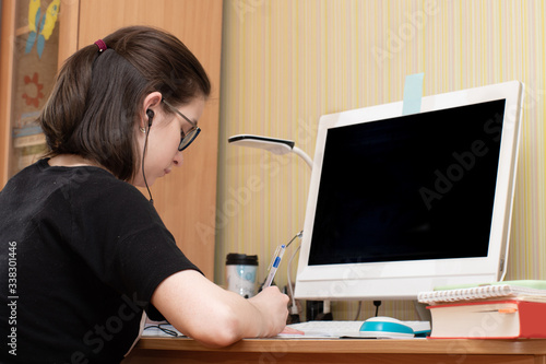 Closeup of a caucasian young woman writes in a notebook in front of a computer with a dark screen. Distance Learning