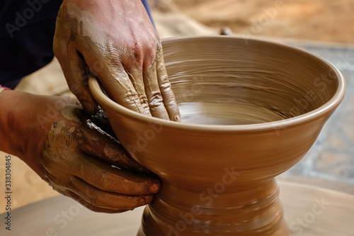 Pottery - skilled wet hands of potter shaping the clay on potter wheel. Pot, vase throwing. Manufacturing traditional handicraft Indian bowl, jar, pot, jug. Shilpagram, Udaipur, Rajasthan, India photo