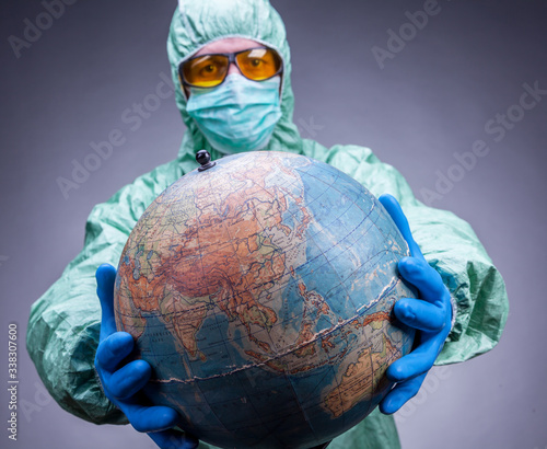 A scientist in a protective suit, blue gloves and yellow glasses holding a glob.