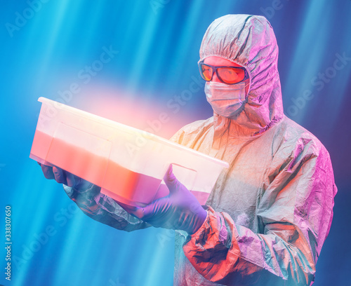 a scientist in a protective suit wearing blue gloves and yellow glasses with a box in his hands.