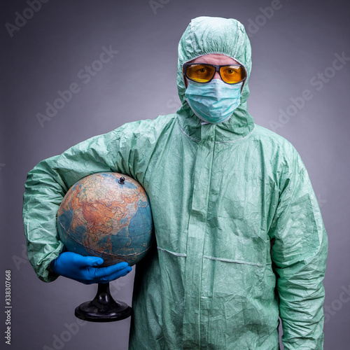 A scientist in a protective suit, blue gloves and yellow glasses holding a glob on the grey background.