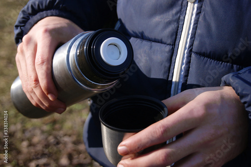 Man's hands pouring fresh hot cocoa from thermos to cup.
