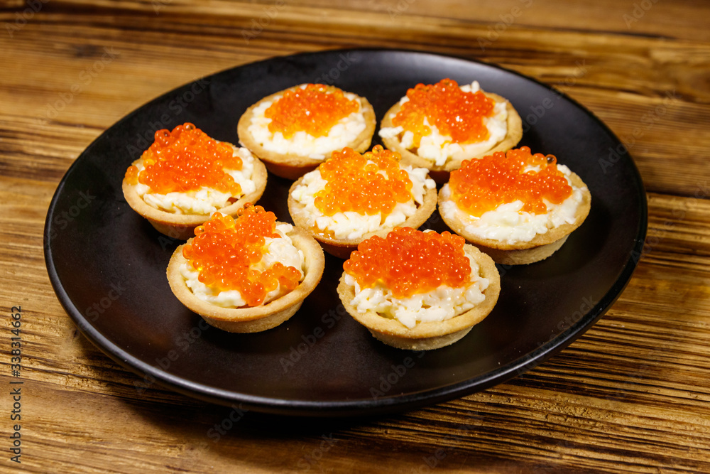 Tartlets with red caviar and soft cheese on a wooden table Tartlets with red caviar and soft cheese on a wooden table