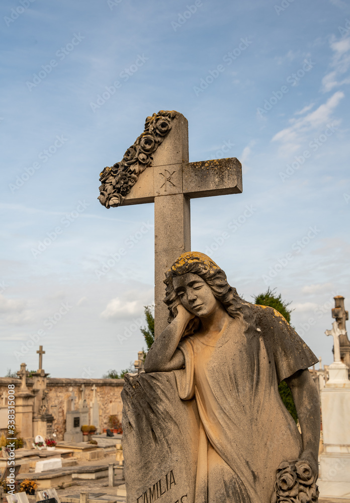 eine Engel stützt sich auf einen Grabstein mit Kreuz  auf einem Friedhof in Spanien