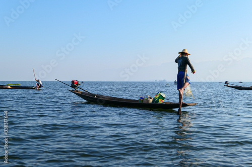 Aisan fisherman on the wooden boat on the lake. Men fishing on the blue river.