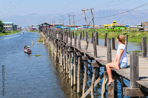 Fotografija Tourist sitting on the wooden bridge over the blue lake