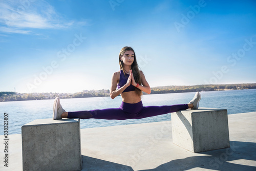 Bild auf Leinwand Side view of a beautiful european  young woman athlete doing the splits while sitting on a warm summer day