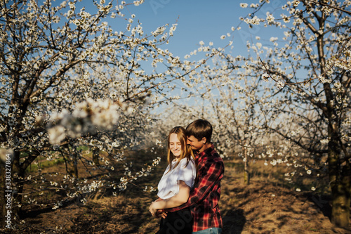 Cute couple embracing in the blooming garden. Tender love feelings. Couple  on blooming trees background. They enjoy spring time. Romantic couple. Young happy couple in love outdoors.