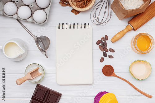 Fototapeta Naklejka Na Ścianę i Meble -  Blank paper notepad with place for text and bakery ingredients and utensils on white table