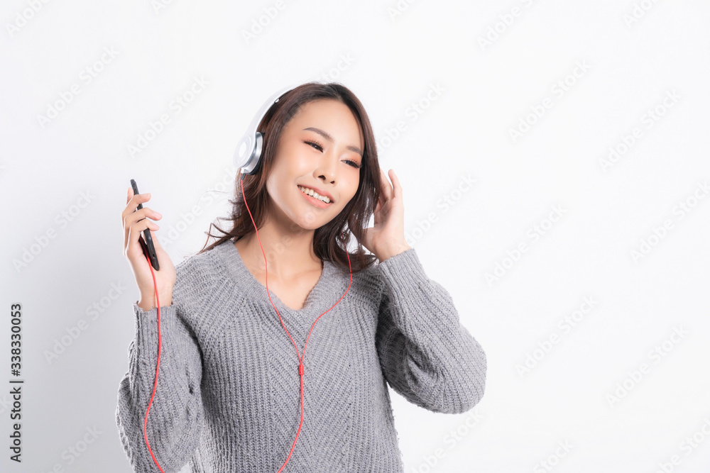 Young beautiful woman wearing a gray sweater is lying and listening to music wearing white music headphones isolated on white background. She is relaxing and happiness Young beautiful woman wearing a gray sweater is lying and listening to music wearing white music headphones isolated on white background. She is relaxing and happiness