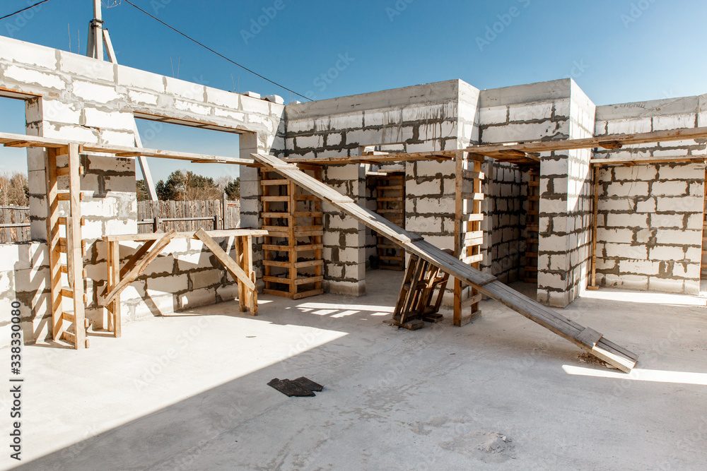 Building site of a house under construction. Unfinished house walls made from white aerated autoclaved concrete blocks. Scaffolding for workers assembled from boards and Euro-pallets. Building site of a house under construction. Unfinished house walls made from white aerated autoclaved concrete blocks. Scaffolding for workers assembled from boards and Euro-pallets.