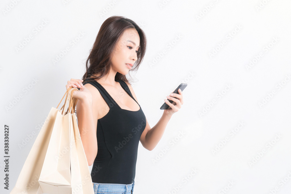 Happy beautiful asian woman black long-haired woman wearing a black shirt, jeans using a mobile phone and carrying shopping bags on isolated gray background, Shopping summer sale concept. Happy beautiful asian woman black long-haired woman wearing a black shirt, jeans using a mobile phone and carrying shopping bags on isolated gray background, Shopping summer sale concept.