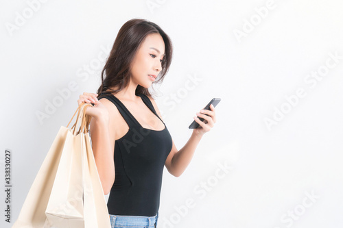 Happy beautiful asian woman black long-haired woman wearing a black shirt, jeans using a mobile phone and carrying shopping bags on isolated gray background, Shopping summer sale concept.