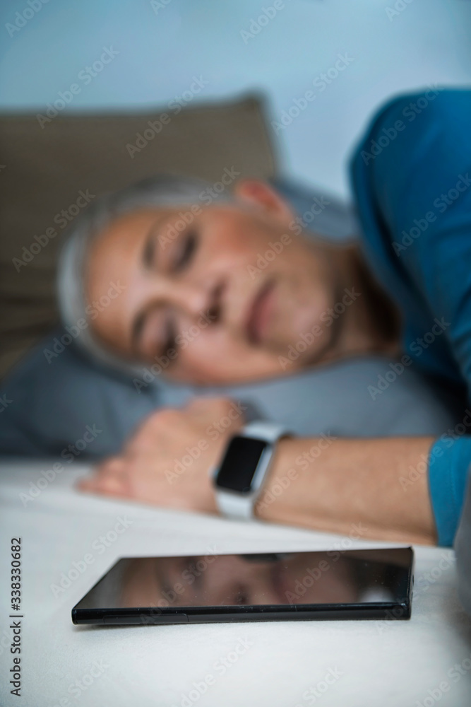 Sleep Apps - Tech-savvy Senior Woman Sleeping in Bed, Using Smart Phone and Smart Watch to Improve her Sleeping Habits Sleep Apps - Tech-savvy Senior Woman Sleeping in Bed, Using Smart Phone and Smart Watch to Improve her Sleeping Habits