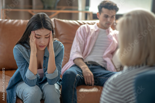 Dark-haired tall man sitting next to his girlfriend and feeling unhappy